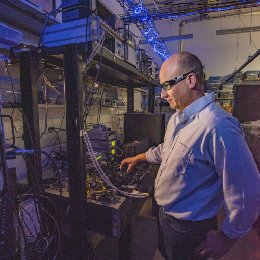 As part of a research project to help establish standards for photon-counting detectors, NIST physicist Thomas Gerrits adjusts the laser beam hitting a detector. The squiggly overhead light helps researchers see the lab setup without disturbing the detectors, which are insensitive to blue light. Credit: J. Burrus/NIST